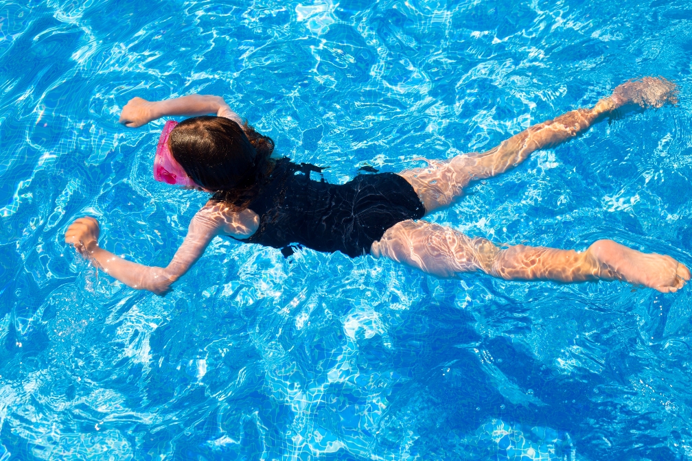 girl with goggles swimming in pool with blue water